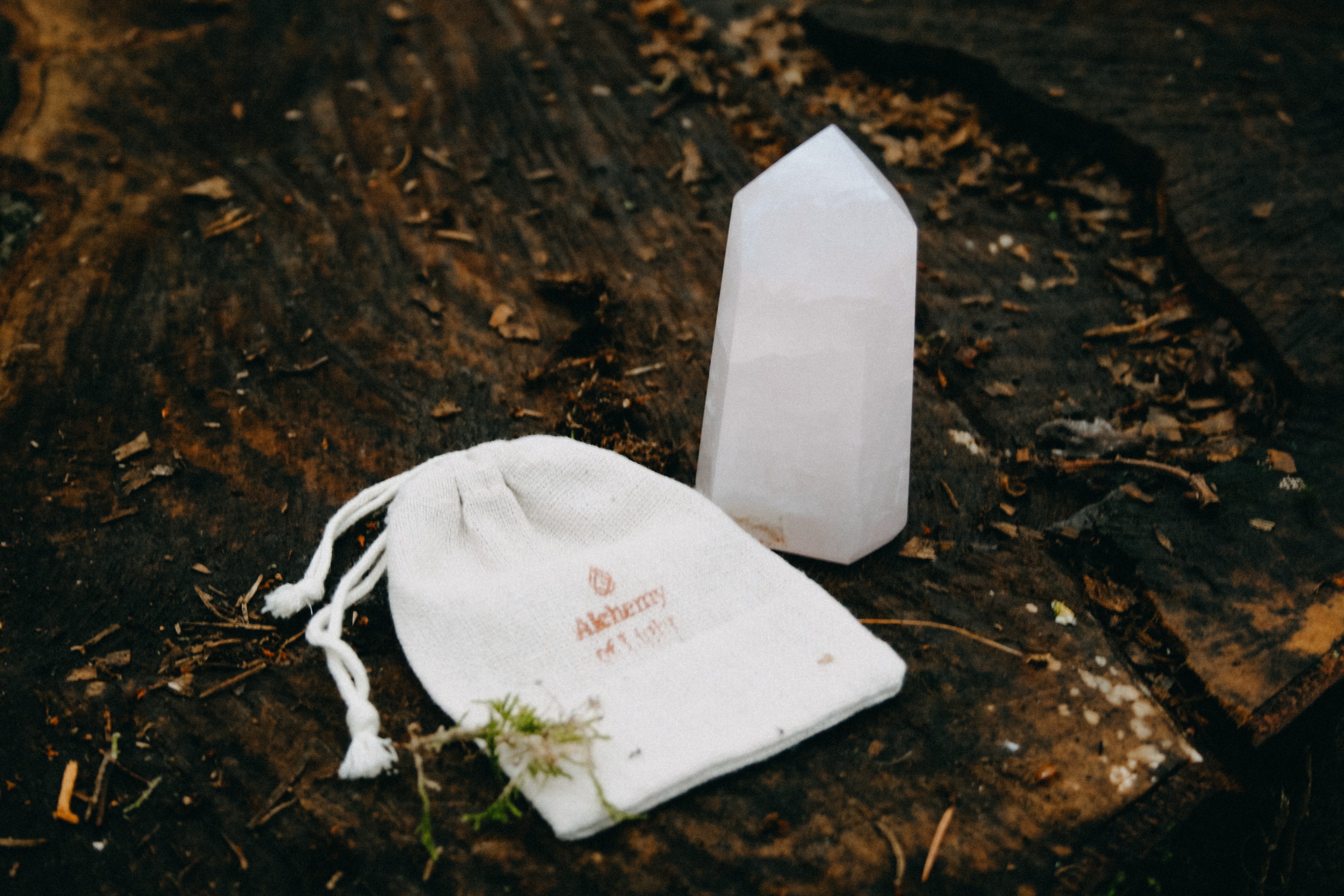 Rozenkwarts Obelisk op houten ondergrond met bijpassend linnen cadeauzakje. Met logo Alchamy of Light