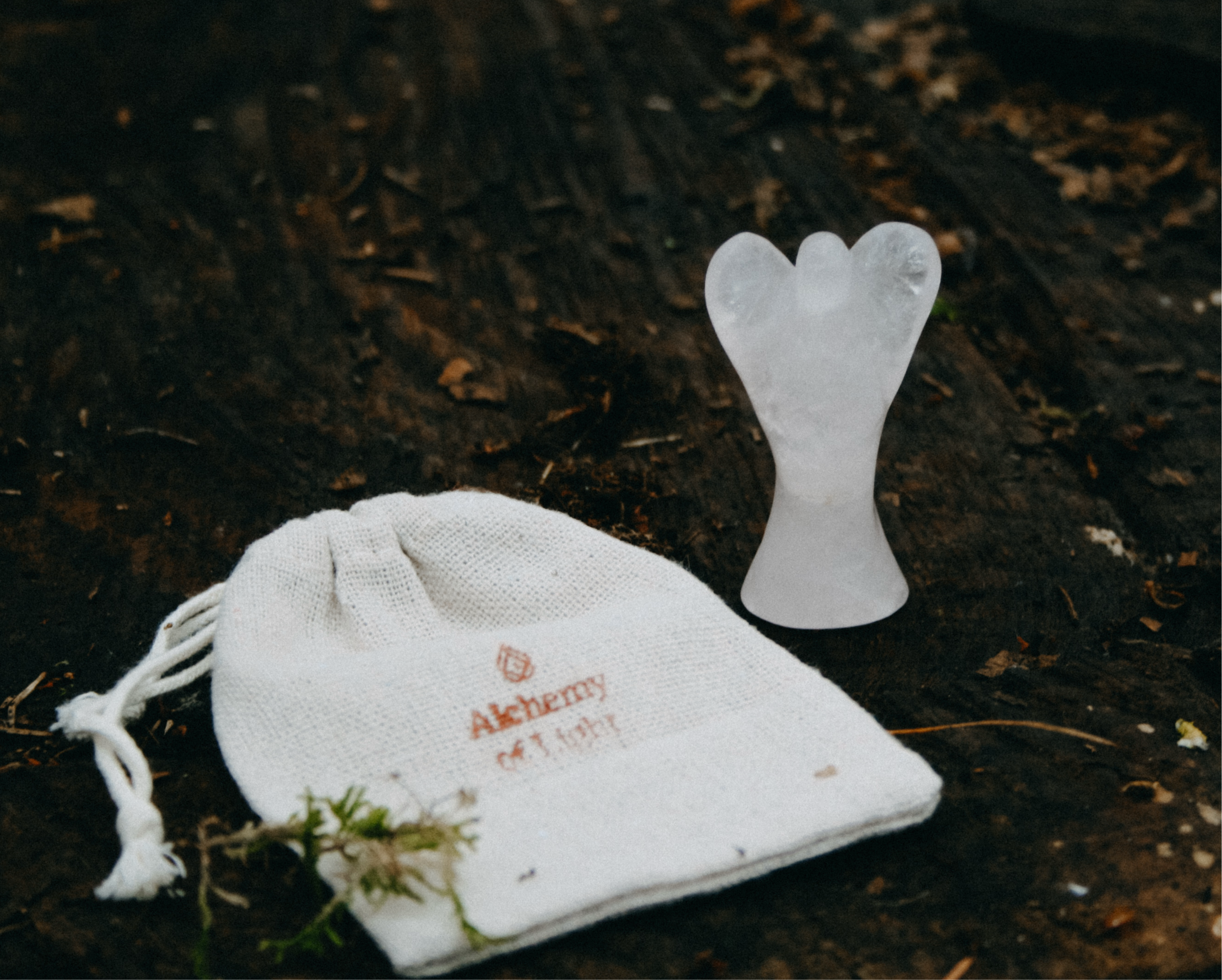 Rozenkwarts engeltje op een houten ondergrond in het bos, met linnen cadeauzakje met logo Alchemy of Light.