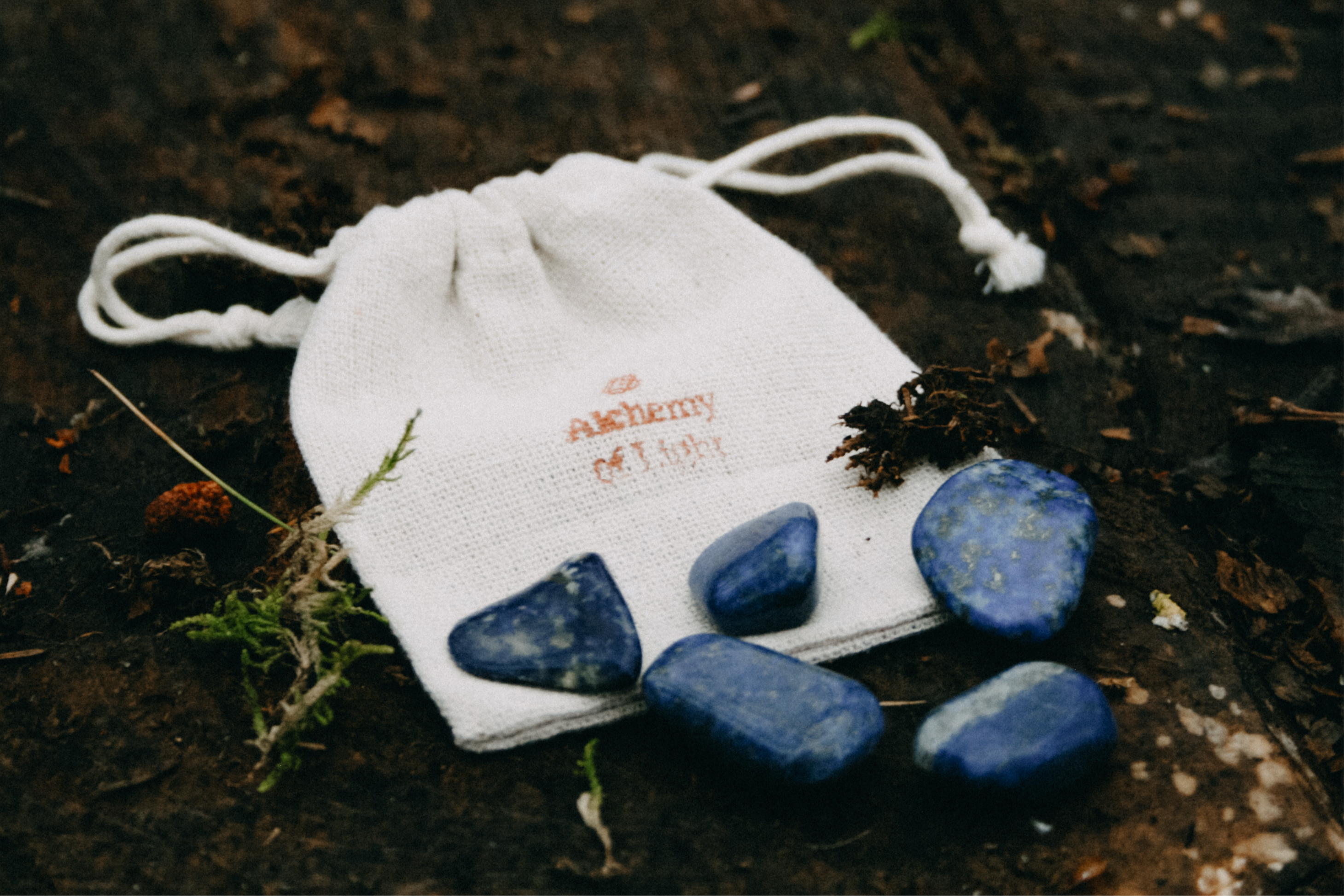 Edelsteen Lapis Lazuli trommelstenen op houten ondergrond - spirituele werking, rust en inzicht. Linnen cadeauzakje met logo Alchemy of Light ligt erbij.